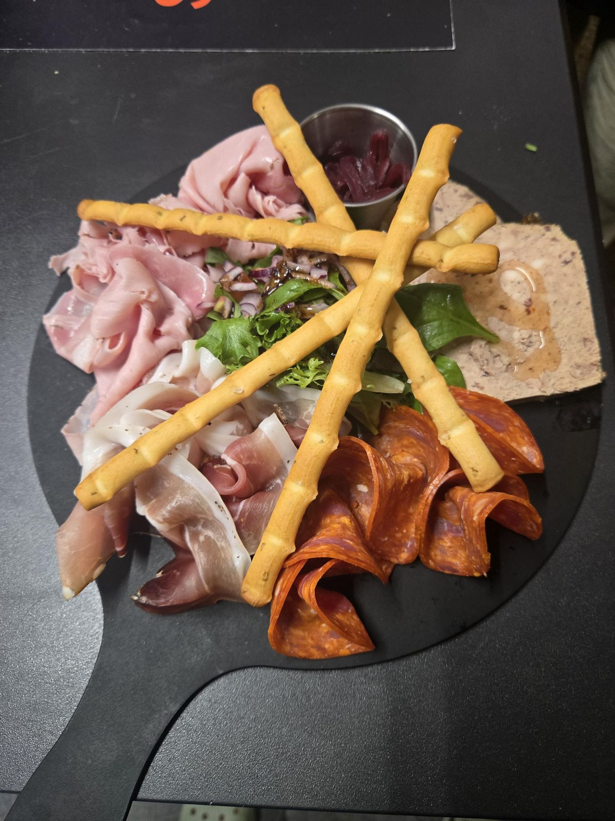 Une planche de jambon blanc, jambon cru, chorizo et pâté, avec des gressins et une petite salade